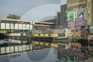 Overground train drives past canal by artists studios and warehouses in Hackney Wick.