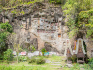 At this burial cliff, condolence signs from past funerals and coffin carriers shaped like traditional Torajan houses are left below the crypts and tao-taos. Tana Toraja, Sulawesi, Indonesia, Asia
