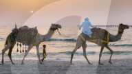 A young boy follows a man riding a horse in Dubai, United Arab Emirates