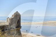 Detail of a watchtower in Cacela Velha, in Algarve, Portugal, with beachgoers crossing a lagoon formed by the low tide.