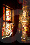 A Tibetan woman stands next to a large prayer wheel of the temple of Boudhanath Stupa, Kathmandu, Nepal