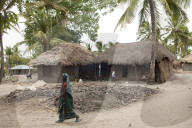A woman walks passed atraditional mud hut home with a solar panel on the top of it.