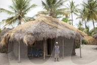 A man stands proudly outside his traditional mud hut home which has just been fitted with a solar panel.