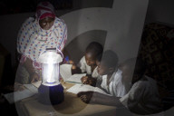 A group of boys read their homework by the light of a solar lantern.