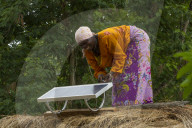 A woman, known as a Solar Mama, fixes a solar panel to the top of a traditional thatched mud hut.