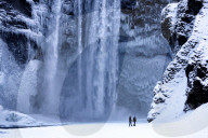 Winter view of Skogafoss waterfall, with cliffs covered in Icicles and foregreound covered in snow, Skogar, South Iceland