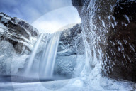 Winter view of Skogafoss waterfall, with cliffs covered in Icicles and foregreound covered in snow, Skogar, South Iceland