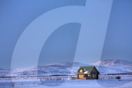 Winter landscape at dusk showing lone cabin bathed in evening sunlight, near Seljalandsfoss, South Iceland