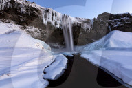 Winter view of Seljalandsfoss Waterfall at dusk with snow covered foreground and icicles hanging from cliffs, South Iceland