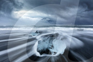 Glacier ice on black sand beach with waves washing up the beach on a stormy winter‚Äôs day, near Jokulsarlon, South Iceland