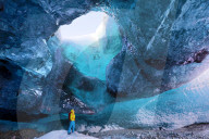 Inside ice cave under the Vatnajokull Glacier, with cave guide looking up to hole in cave roof, near Jokulsarlon, South Iceland