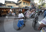 Old style running rickshaw wallah pulling woman and her shopping through Kolkata streets away from the Kali temple, West Bengal