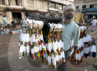 Man in head scarf selling girls' dresses from a rack he carries on his shoulder in the main street in Puri, Odisha