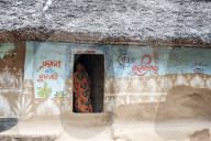 Woman at the door of traditional mud walled Odisha village house decorated with traditional Odishan patterns, Dandasahi, Odisha