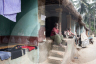 Men sitting chatting in the afternoon on the verandahs of their traditional thatch and brick built village homes, rural Odisha