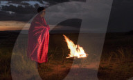 Portrait Masai Mara man wearing traditional tribal red blanket by camp fire, Masai Mara National Park, Kenya.