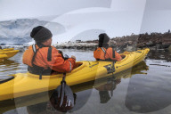 Couple kayaking in the snow, watching a Gentoo penguin colony, Chilean Gonzalez Videla Station, Waterboat Point, Antarctica