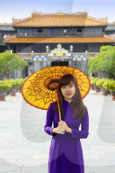 Woman in a traditional Ao Dai dress with a paper parasol in the Forbidden Purple City of Hue, A Unesco World Heritage Site