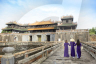 Women in traditional Ao Dai dresses with a paper parasol in the Forbidden Purple City of Hue, A Unesco World Heritage Site