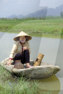 Local village fisher woman wearing a Non La conical hat and sitting in a concrete lined bamboo boat