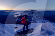 Hiker on snowy peak looks towards bridge and sea, Sommaroy island, Troms county, Norway