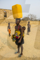 Woman with her baby on the back carrying a water canister on her head, Massangano, Cuanza Norte, Angola
