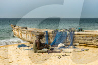 Man fixing their nets in their fishing boats on a beach in Robertsport, Liberia