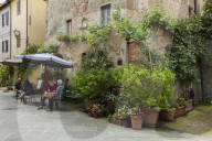 People sitting outside at a restaurant within a small courtyard surrounded by flowers in Pienza
