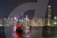 Traditional junk boat on Victoria Harbour with city skyline behind illuminated at night, Hong Kong