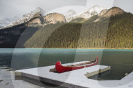 Red canoe and dock in Lake Louise with snow-covered mountains, Banff National Park, Alberta, Canada