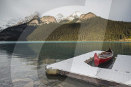 Red canoe and dock in Lake Louise with snow-covered mountains, Banff National Park, Alberta, Canada