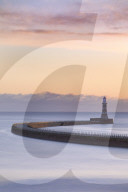 The colours of a winter sunrise over the curving pier and lighthouse at Roker, Sunderland on the North East Coast, UK