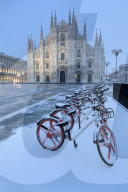 Parked bicycles covered by snow in PIazza Duomo. Milan, Lombardy, Northern Italy, Italy.