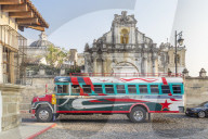 A typical colorful painted chicken bus passing at the entrance gate of San Francisco Church in Antigua