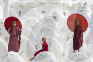 Three young monks dressed in red, with red parasols at the Myatheindan Pagoda (White Temple) in Mingun, Myanmar (Burma)