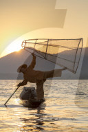 A fisherman standing on one leg and holding his fishing net at sunset on Inle Lake, Myanmar (Burma), Asia