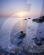 A colourful spring sunrise over Torbay with warm light glinting off the wet rocks, Anstey's Cove, Torquay, Devon, UK