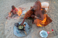 One senior red ochred, Himba woman with her child cooking on an open fire, Puros Village, nr Sesfontein, Namibia (Model Release)
