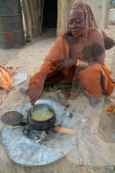 One senior red ochred, Himba woman cooking her meal on an open fire, Puros Village, near Sesfontein, Namibia (Model Release)