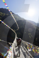 Asia Nepal Khumbu valley Sagamartha National Park Unesco, porter crossing a suspension bridge decorated in Tibetan prayer flags