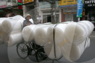 Man pedals a trishaw, loaded with rolls on a road. Ho Chi Minh City. Vietnam.