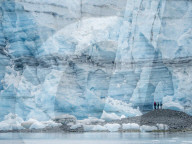 Hikers in front of Lamplugh Glacier, Glacier Bay National Park and Preserve, Alaska, USA.