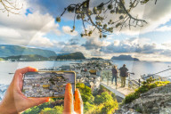 Hands holding smartphone photographing Alesund from Byrampen viewpoint, More og Romsdal county, Norway