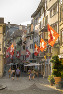 Tourists look at the Swiss Flags hanging from buildings in Lindenhof, Zurich, Switzerland