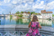 Rear view of woman leaning on terrace over Limmat River admiring the old buildings of Lindenhof, Zurich, Switzerland