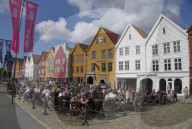 Tourists sit in the sun in outdoor bars and cafes in the old wharf and traditional wooden buildings in the Bryggen quarter of Bergen,Norway