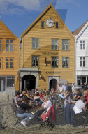 Tourists sit in the sun in outdoor bars and cafes in the old wharf and traditional wooden buildings in the Bryggen quarter of Bergen,Norway