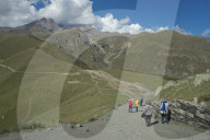 Tourists near the Gergeti Holy Trinity Church by the river Chkheri, under Mount Kazbegi at an elevation of 2170 meters in the Caucasus, Georgia