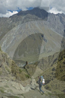 Tourists trekking near the Gergeti Holy Trinity Church by the river Chkheri, under Mount Kazbegi at an elevation of 2170 meters in the Caucasus, Georgia
