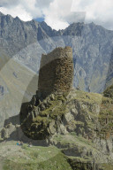 Tourists trekking by a tower near the Gergeti Holy Trinity Church by the river Chkheri, under Mount Kazbegi at an elevation of 2170 meters in the Caucasus, Georgia